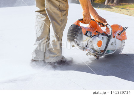 Masonry contractor is using concrete saw to cut through surface while dust clouds form around saw feet. Masonry contractor is using concrete saw to cut through surface while dust clouds form around saw feet. 141589734