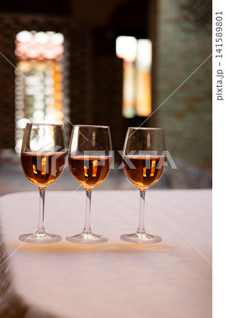 Three stemmed glasses filled with an amber-colored alcoholic beverage arranged on a restaurant table. Elegant still life with rose pink wine. 141589801