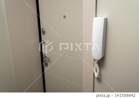 Door intercom unit is mounted beside a closed door in a hallway setting 141589842