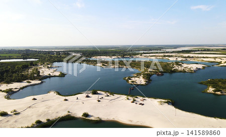 Aerial view of a sand quarry with multiple blue lakes and white sand shorelines, showing industrial water excavation Aerial view of a sand quarry with multiple blue lakes and white sand shorelines, showing industrial water excavation 141589860