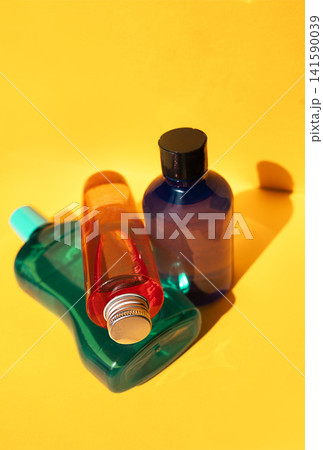 Three colorful plastic bottles in various shapes and sizes positioned on a bright yellow background, showcasing vibrant hues of green, red, and blue 141590039
