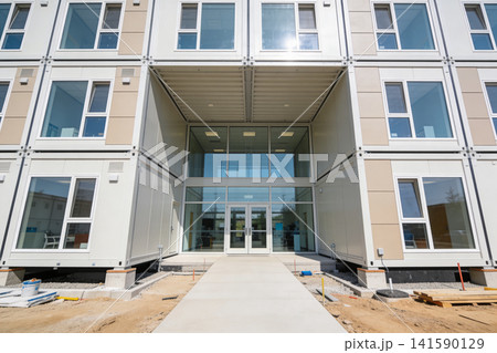 Modern modular building entrance with stacked shipping container units and large glass facade Modern modular building entrance with stacked shipping container units and large glass facade 141590129