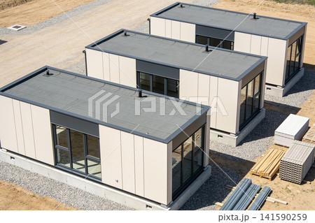 Modern modular homes under construction on a gravel lot with building materials nearby Modern modular homes under construction on a gravel lot with building materials nearby 141590259