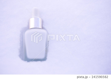 Clear glass dropper bottle with silver cap resting in fresh white snow, showcasing a minimalist design against a winter landscape background Clear glass dropper bottle with silver cap resting in fresh white snow, showcasing a minimalist design against a winter landscape background 141590382