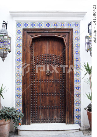 Ornate wooden door with intricate carvings and decorative tiles, flanked by lanterns and potted plants in a traditional architectural setting 141590423