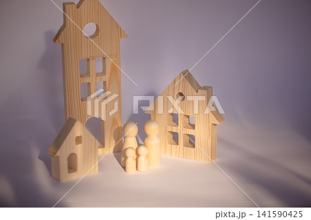 Wooden toy houses and figurines arranged on a light background, showcasing various shapes and sizes of houses and family figures in a playful setting 141590425
