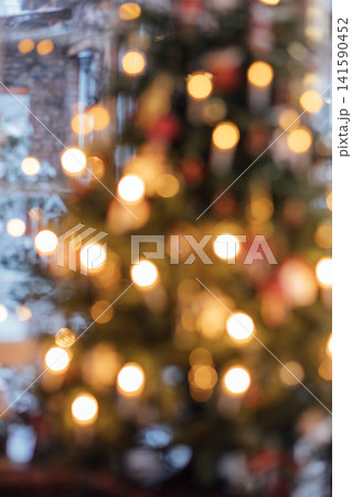 Blurred view of a decorated Christmas tree with glowing lights and ornaments, creating a festive atmosphere in a cozy indoor setting Blurred view of a decorated Christmas tree with glowing lights and ornaments, creating a festive atmosphere in a cozy indoor setting 141590452