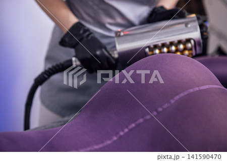 Female therapist using a massage device on a purple upholstered chair, demonstrating relaxation techniques in a soothing environment with soft lighting and modern decor Female therapist using a massage device on a purple upholstered chair, demonstrating relaxation techniques in a soothing environment with soft lighting and modern decor 141590470