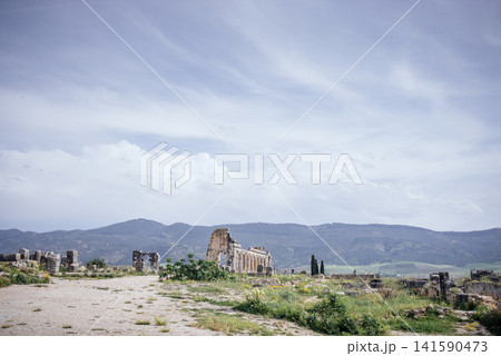 Ancient ruins of a historical site surrounded by lush greenery and mountains under a cloudy sky, showcasing the beauty of nature and heritage in a serene landscape Ancient ruins of a historical site surrounded by lush greenery and mountains under a cloudy sky, showcasing the beauty of nature and heritage in a serene landscape 141590473