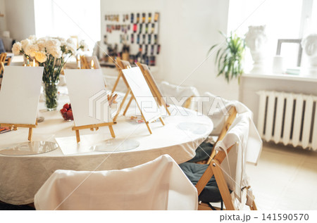 A room for a master class in gouache or acrylic painting. A table with a tablecloth and easels with canvases and plastic palettes. A room for a master class in gouache or acrylic painting. A table with a tablecloth and easels with canvases and plastic palettes. 141590570