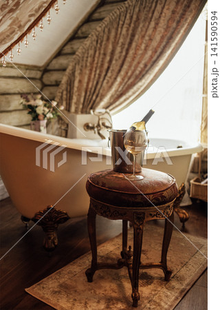 Close-up of a glass of wine and a bottle in an ice bucket on an elegant chair in the bathroom Close-up of a glass of wine and a bottle in an ice bucket on an elegant chair in the bathroom 141590594