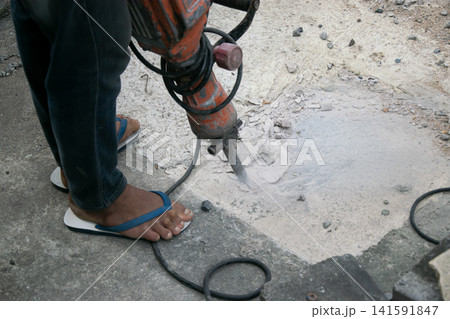 The workers are drilling into the ground without wearing safety shoes. 141591847