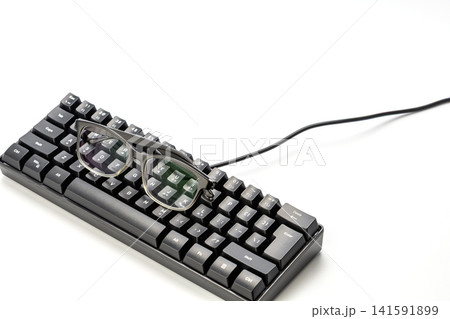 Pair of black framed prescription eyeglasses resting on top of a compact black mechanical gaming keyboard with cable, isolated on a clean white background, representing nearsighted computer user idea Pair of black framed prescription eyeglasses resting on top of a compact black mechanical gaming keyboard with cable, isolated on a clean white background, representing nearsighted computer user idea 141591899
