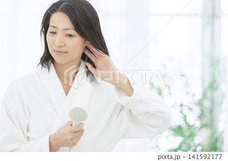 バスローブ姿で髪を乾かす中年女性 バスローブ姿で髪を乾かす中年女性 141592177