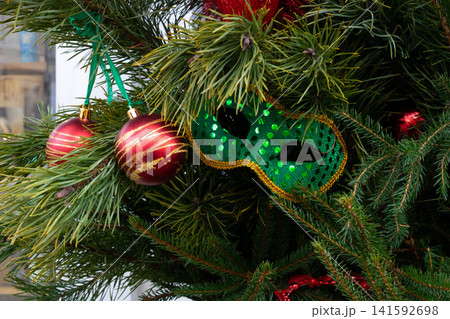 A green carnival mask lies on the Christmas tree branches, and New Year's toys are hanging. The concept of Christmas and New Year A green carnival mask lies on the Christmas tree branches, and New Year's toys are hanging. The concept of Christmas and New Year 141592698