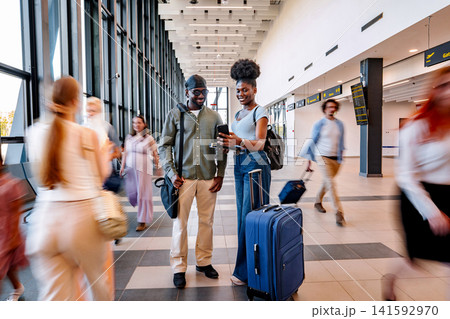 Traveling couple checking smartphone in busy airport terminal Traveling couple checking smartphone in busy airport terminal 141592970
