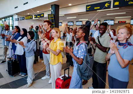 Diverse travelers applauding at airport terminal gates Diverse travelers applauding at airport terminal gates 141592971