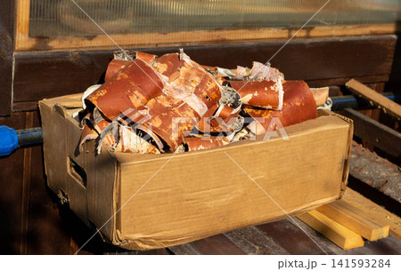 Birch bark is stored in a cardboard box on a pile of wood. Dried bark is used for lighting fires in fireplaces or stoves. Birch bark is stored in a cardboard box on a pile of wood. Dried bark is used for lighting fires in fireplaces or stoves. 141593284