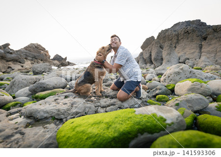 Man plays with dog on rocky beach during sunset near the ocean Man plays with dog on rocky beach during sunset near the ocean 141593306