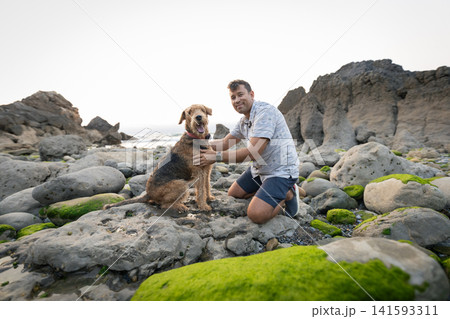 Dog and owner explore rocky shoreline during sunset Dog and owner explore rocky shoreline during sunset 141593311