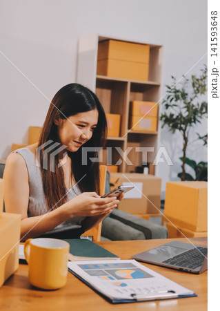 Startup SME small business entrepreneur of freelance Asian woman wearing apron using laptop and box to receive and review orders online to prepare to pack sell to customers, online sme business ideas. Startup SME small business entrepreneur of freelance Asian woman wearing apron using laptop and box to receive and review orders online to prepare to pack sell to customers, online sme business ideas. 141593648