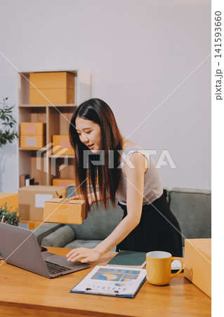 Startup SME small business entrepreneur of freelance Asian woman wearing apron using laptop and box to receive and review orders online to prepare to pack sell to customers, online sme business ideas. 141593660