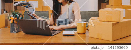 Startup SME small business entrepreneur of freelance Asian woman wearing apron using laptop and box to receive and review orders online to prepare to pack sell to customers, online sme business ideas. 141593669