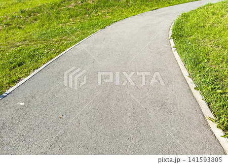 Curved asphalt pathway bordered by green grass in a sunny outdoor park setting Curved asphalt pathway bordered by green grass in a sunny outdoor park setting 141593805