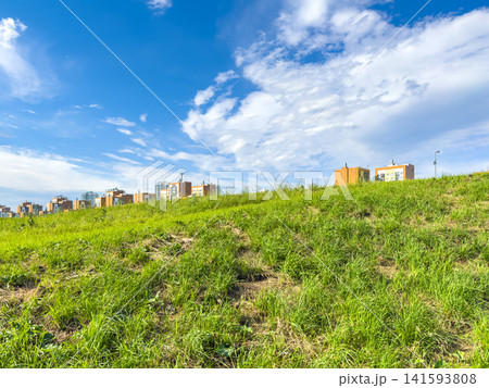 Green hillside with residential buildings under a bright blue sky and scattered clouds Green hillside with residential buildings under a bright blue sky and scattered clouds 141593808
