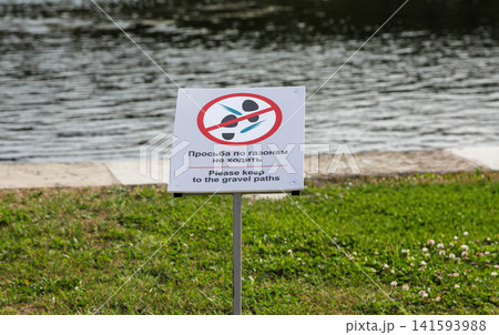 Sign on lawn with Russian text keep off the grass. Warning notice on urban embankment grassy area. Public park rule signage Sign on lawn with Russian text keep off the grass. Warning notice on urban embankment grassy area. Public park rule signage 141593988