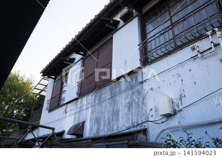 塗装が剥げた白い波板トタンの外壁と格子窓が並ぶ古い木造建築の外観 塗装が剥げた白い波板トタンの外壁と格子窓が並ぶ古い木造建築の外観 141594023