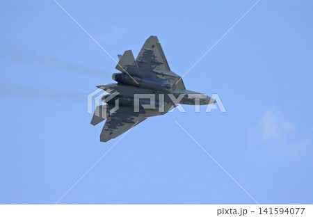 Russia Kubinka 12 April 2025. Su-57 fifth generation fighter jet performing aerobatics during an air show. Russian stealth aircraft in flight with smoke trails against blue sky 141594077