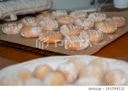 Freshly baked almond cookies dusted with powdered sugar cool on baking paper while homemade cookie dough waits in foreground. Home baking, dessert, recipe, confectionery, food preparation, culinary Freshly baked almond cookies dusted with powdered sugar cool on baking paper while homemade cookie dough waits in foreground. Home baking, dessert, recipe, confectionery, food preparation, culinary 141594132