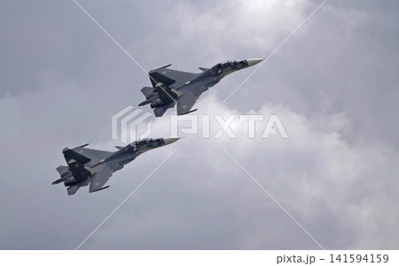 Russia Kubinka 12 April 2025. Pair of Su-30SM fighter jets performing aerobatics during an air show. Two Russian military aircraft in formation flight with smoke trails against blue sky 141594159