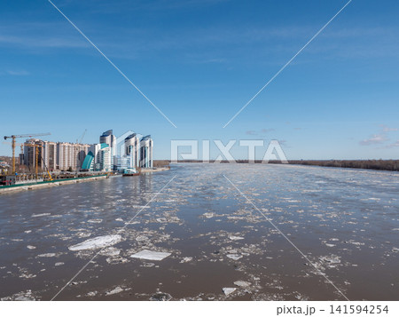 April 09 2026 Barnaul Russia aerial view of Ob River ice drift floating ice with new high-rise buildings near River Station spring cityscape urban development. 141594254
