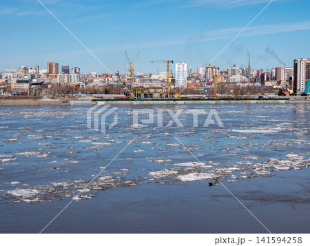 April 09 2026 Barnaul Russia aerial view of Ob River ice drift floating ice with new high-rise buildings near River Station spring cityscape urban development. 141594258