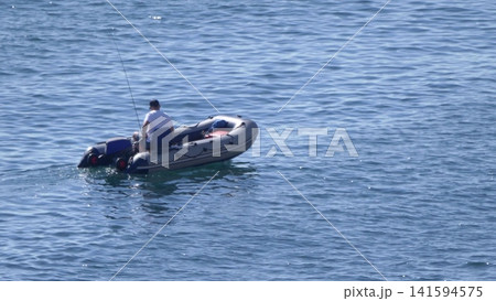 A fisherman in an inflatable boat on the sea. Calm water, clear sky, peaceful maritime scene A fisherman in an inflatable boat on the sea. Calm water, clear sky, peaceful maritime scene 141594575