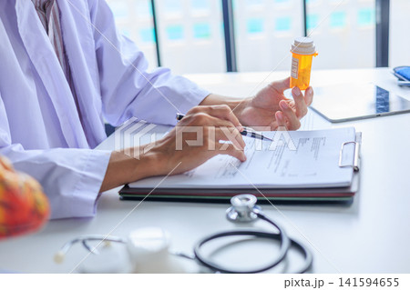 Doctor writing prescription order and holding medication bottle at desk in clinic. Doctor writing prescription order and holding medication bottle at desk in clinic. 141594655