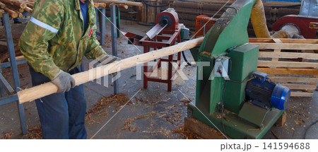 A worker feeds a long wooden pole into a green industrial woodworking machine 141594688