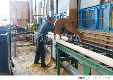 A blurred worker operates machinery in a sawmill A blurred worker operates machinery in a sawmill 141594689