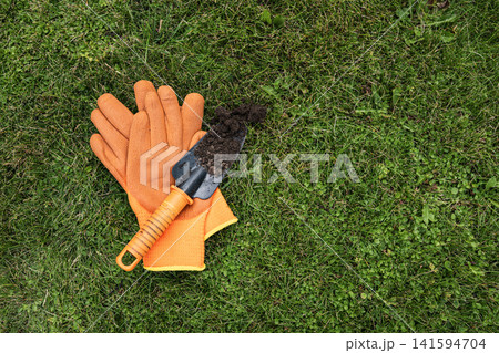 Gardening gloves and hand trowel with soil on green grass top view Gardening gloves and hand trowel with soil on green grass top view 141594704