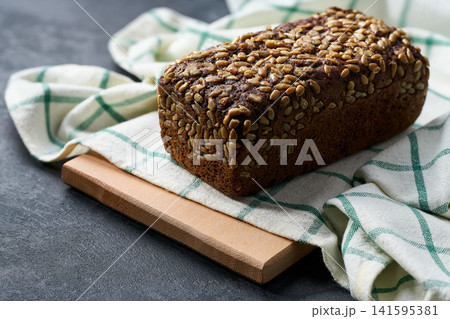 loaf of freshly baked wholemeal rye bread with sunflower seeds on dark kitchen table, selective focus. 141595381