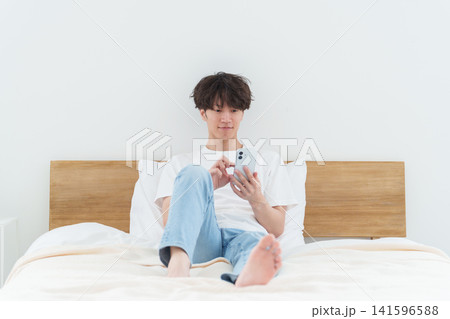 ベッドでスマートフォンを使う男性 ベッドでスマートフォンを使う男性 141596588