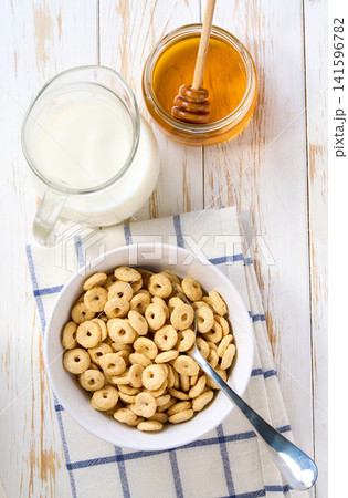 corn rings in a ceramic bowl with milk and honey on a white wooden table, top view. corn rings in a ceramic bowl with milk and honey on a white wooden table, top view. 141596782