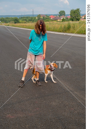 Teen girl standing with beagle dog on asphalt road 141597696