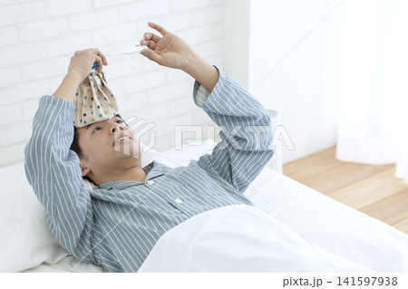 ベッドで体温を測るパジャマ姿の男性 141597938