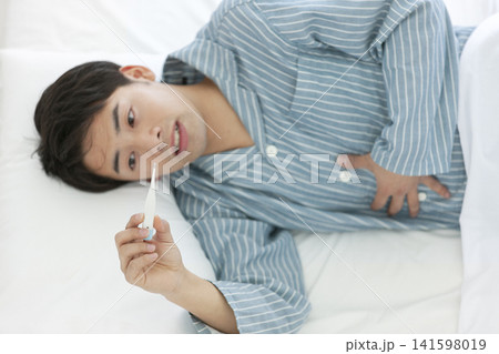 ベッドで体温を測るパジャマ姿の男性 ベッドで体温を測るパジャマ姿の男性 141598019