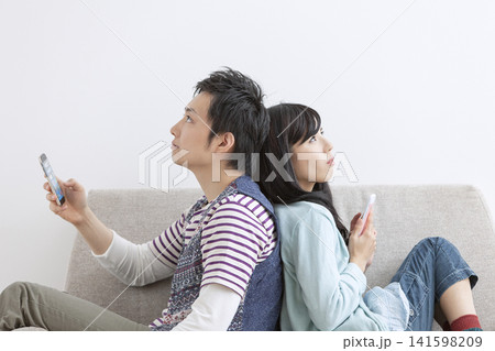 ソファで携帯電話を見る夫婦 ソファで携帯電話を見る夫婦 141598209