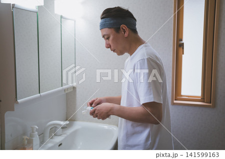 洗面所でヘアバンドをして歯ブラシに歯磨き粉をつける40代男性 洗面所でヘアバンドをして歯ブラシに歯磨き粉をつける40代男性 141599163