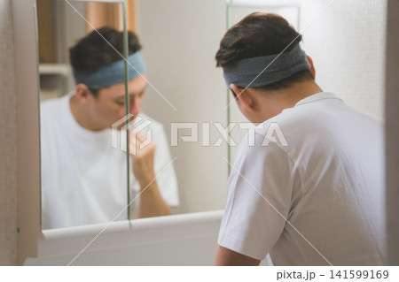 洗面所でヘアバンドをして歯磨き中の40代男性 洗面所でヘアバンドをして歯磨き中の40代男性 141599169